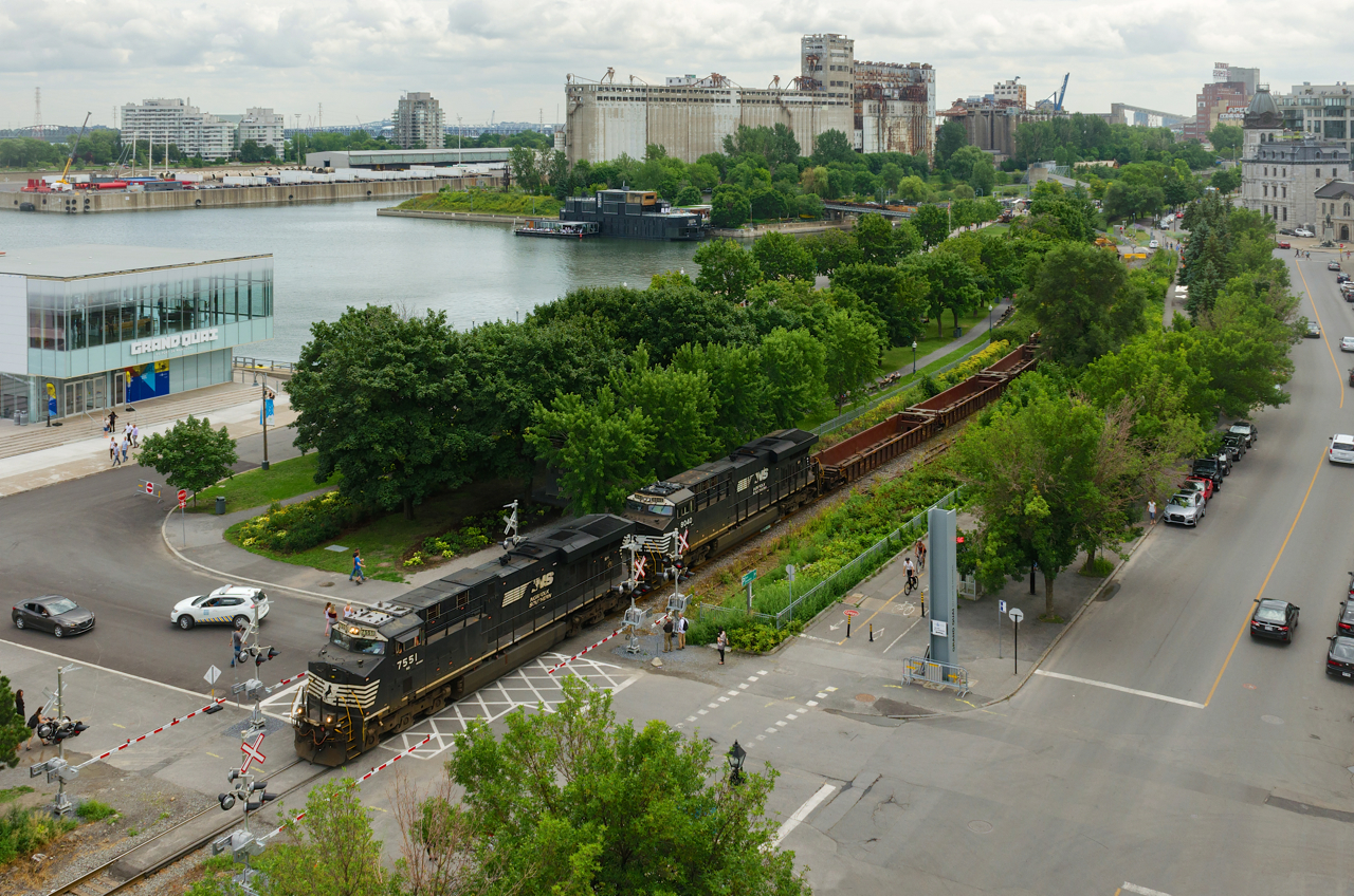 GEVO's NS 7551 & NS 8040 lead CN 543 into the Port of Montreal with baretables as they go over a crossing with newly installed gates. In the background at right is the out of use grain elevator #5.