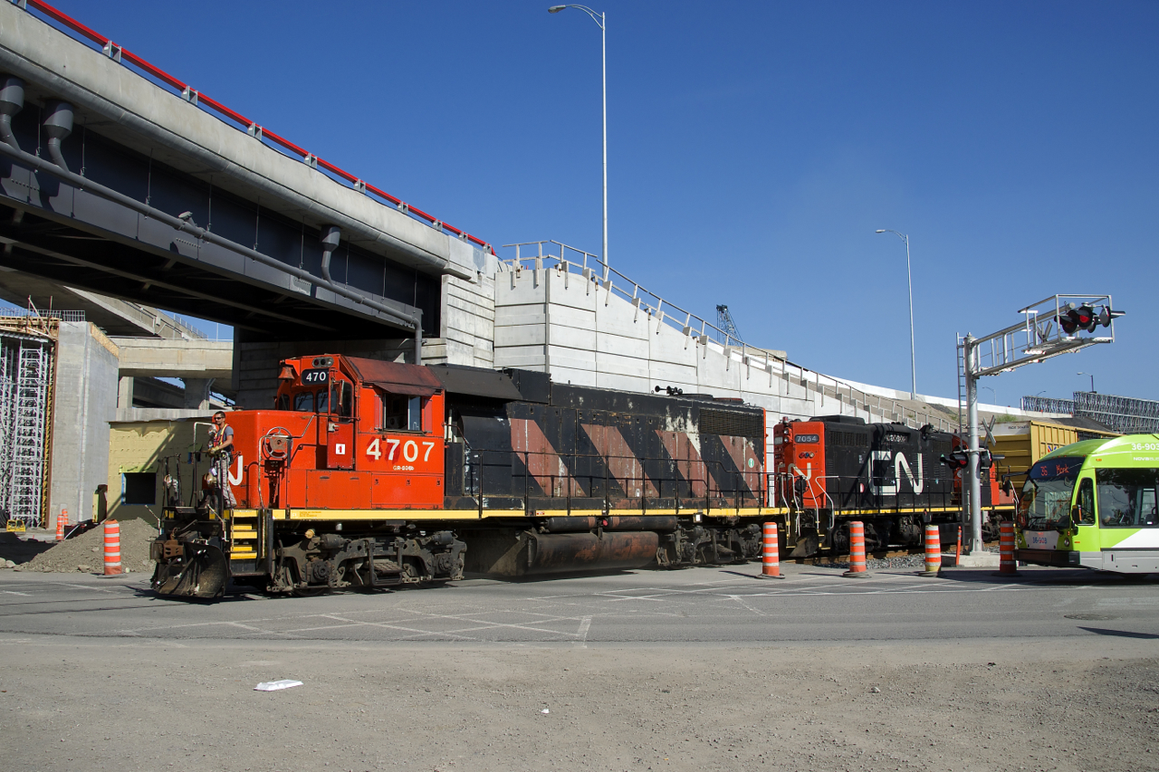 With a single boxcar for the Kruger plant, the Pointe St-Charles Switcher with CN 4707 & CN 7054 for power is crossing Notre-Dame street on the rarely used Turcot Holding Spur. It is passing under a new section of the Turcot interchange, as part of that infrastructure project, the track and crossing here were completely redone during the last year or two.