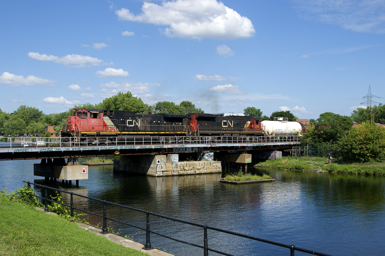 Canadian cab CN 2522 and standard cab CN 2122 lead CN 527 over the Lachine Canal on a hot summer afternoon in Montreal. This edition of CN 527 is going straight from Southwark Yard to Taschereau yard, foregoing its usual work at the nearby Pointe St-Charles Yard.