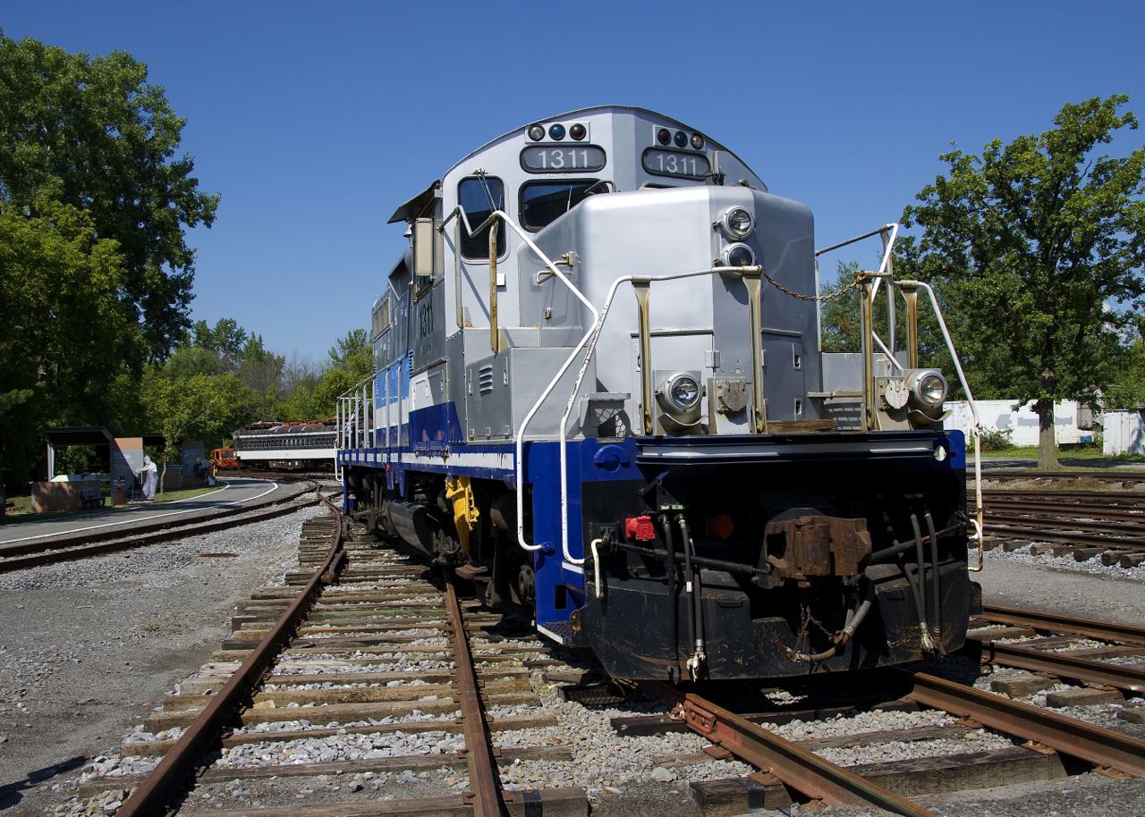 GP9 AMT 1311 basks in the sun at Exporail, with a CN MU car in the background at left.
