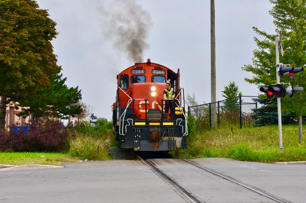 After finishing a few of the minor switching tasks in BIT near Queen st, CN gp9rm 7264 has throttled up and ran about a mile north to lift a long set of intermodel cars likley set out by CN 148 earlier in the afternoon on the second main track. In this scene here the geep is throttling up (as you can see from the steam-like substance coming out of the top of the unit) and will run the train north for a mile or so to allow the rear of the train to clear a switch that leads off the main into BIT. 7264 will then reverse the mammoth train into BIT so the containers can be unloaded.   The crossing I was standing at is Ward rd and just south of the crossing is where the single track pullback line splits into 3 track and just a mile south of here on the east lies the busy Brampton Intermodel Terminal.   The Industrial building hidden on the left known as T&T Marble Granite is one of the many industries that reside in this area. Kind of a funny fact, this 2-3 mile pullback track is known as the North Park Industrial Lead but for a long time it did not service any of the industries in this area. It was used as a pullback for the intermodel trains and nothing more. The pullback line ends at Chrysler who intended to use rail service right when they were built in the mid 80s but some particular ‘noise issues’ got in the way. Late in 2014 however, they added a new facility next to their plant to ship automobiles out by rail and that operating seems to be a success as to the present day CN still makes a trip to their plant for autoracks several times a week early in the morning and there seems to be no complaints about any noise.