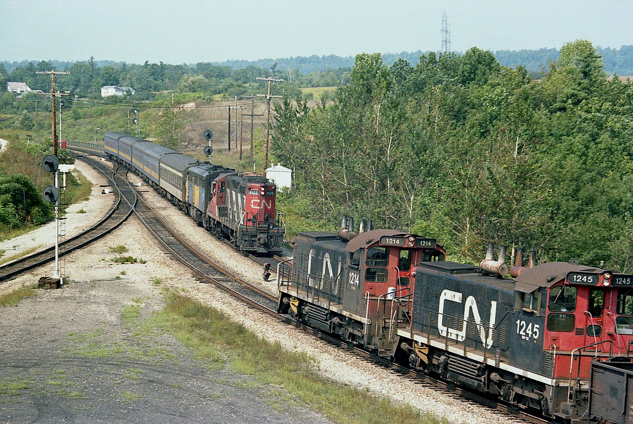 This is actually a three-way meet. That is, if you want to count that little motor car half obscured in the curve over the Hwy 403. :o) CN 1214 and 1245 with a very short train (3 cars and caboose 79382) awaits the eastbound CN 4105 and VIA 6779 as seen from the hillside at what was referred to as Hamilton West back then.
