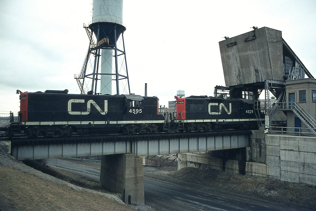 CN local has just worked Merritton's small yard and is heading back to Niagara Falls in this early March view. The mucky snow is melting away and the scenery can only get better. CN 4529 leads sister 4595 eastward over the Welland Canals Parkway and the canal itself. Chimney and water tower in the far background are part of the Glendale GM plant.