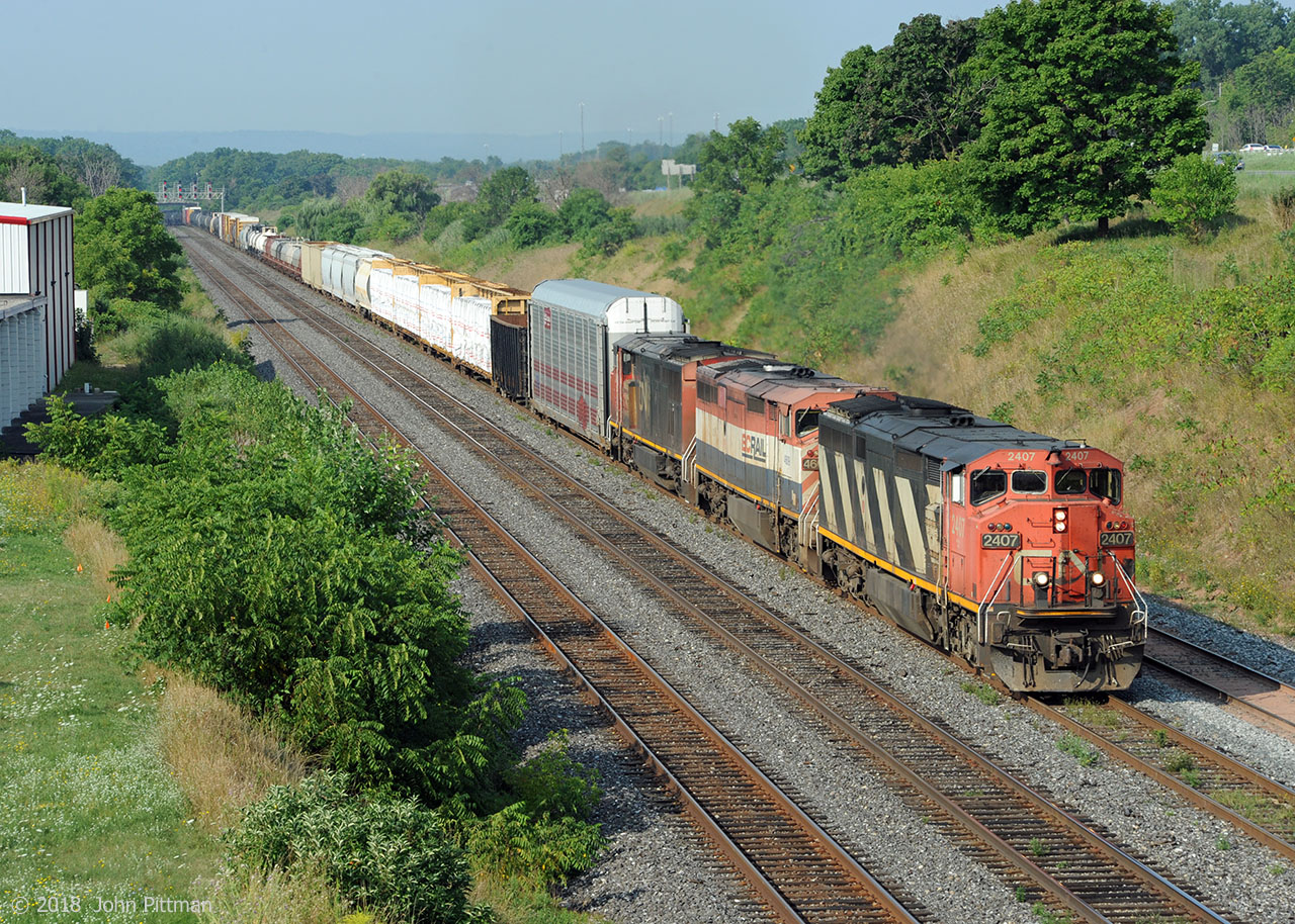 Three Draper taper cowl GE Dash 8-40CM units power CN 422 eastward on Oakville Sub track 1. They wear their original colour schemes - CN diagonal stripes, BC Rail, CN North America.East-side signals for CN Snake can be seen 1km back.  Alongside is the west lead to/from Aldershot Yard; 422's crew will make a small setoff and a much larger lift from Aldershot East.  Notable in August 2018 has been the absense of high-cube auto parts boxcars on 422; possibly Ford Oakville is retooling for the 2019 model year.