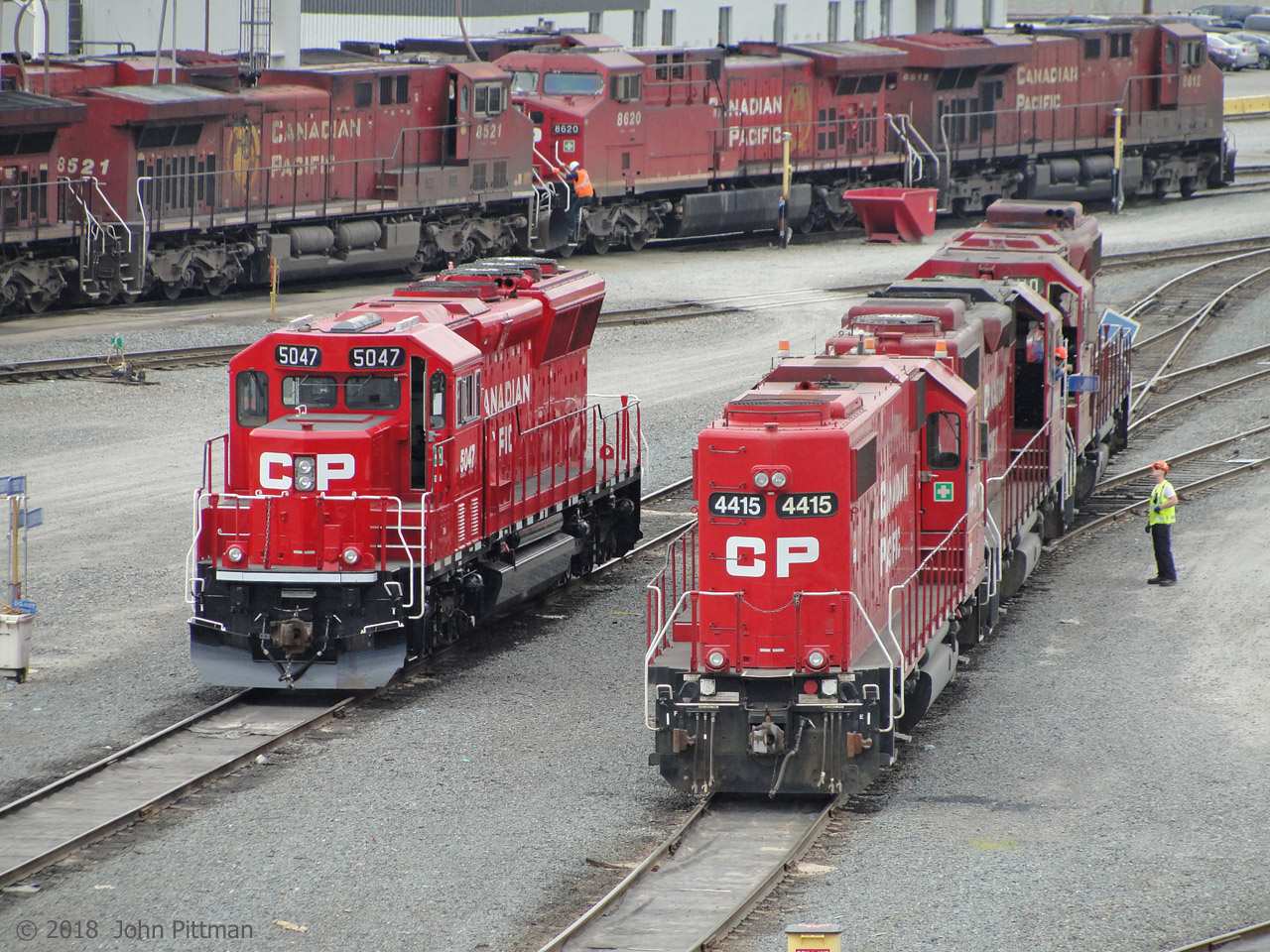 EMD-family locomotives getting attention outside the diesel shop, with GE units at the sand/fuel area beyond. 
SD30C-ECO CP 5047 in clean glossy paint is shutdown near three GP38-2's SOO 4415, CP 3090, CP 3110. Further away are GE AC4400's CP 8521 and CP 8620, with ES44AC CP 8812 rightmost. 
Vantage point is the Coast Meridian Overpass (bridge) - great views of CP Port Coquitlam Yard, annoying security mesh.