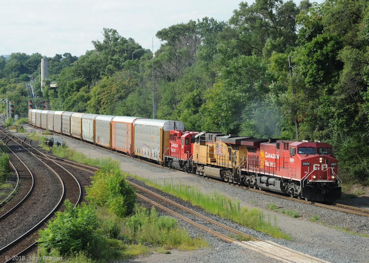 CP 8601 (AC4400) in clean paint with the new beaver emblem leads a CP freight train north on the Hamilton Sub assisted by UP 5550 (ES44ac with UP class AC45CCTE) and CP 2211 (GP20C-eco). Most of the train is still on the other side of Hamilton's High Level Bridge. North-side Desjardins (canal) signals are behind the last visible autorack. CN's Cowpath and Hamilton Junction are alongside. 
CP2211 has often been part of a helper set - this train will go up the hill with just the power seen here.