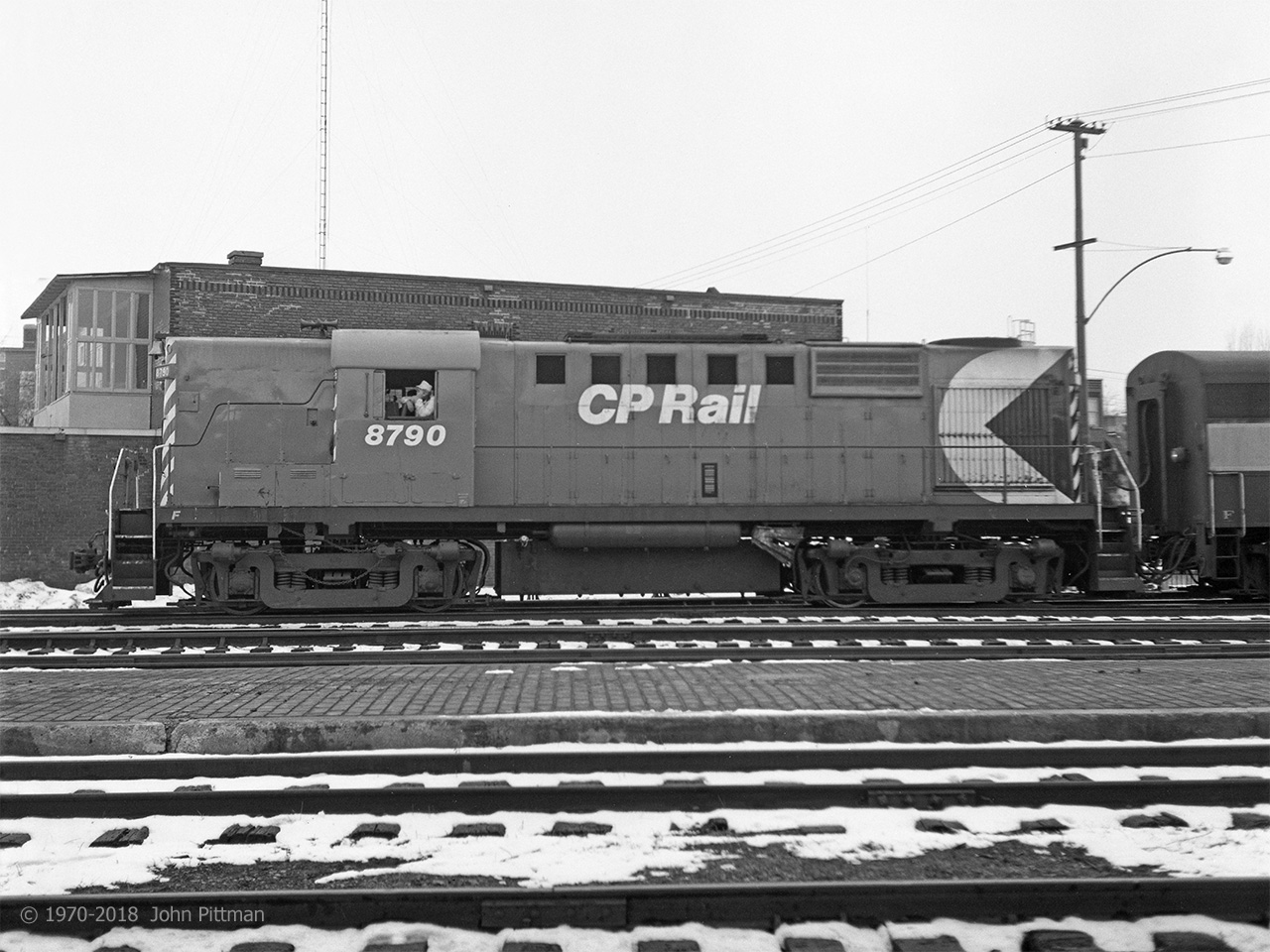 Clean and glossy in fresh CP Rail paint, the crew of MLW RS-18 CP 8790 awaits clearance to take their train eastward to Montreal one afternoon in the winter of 1970-71. Behind it is a CP MLW FB or FB-2. 
The posture of the crewman on the left is expressive, and his hat would go well with a steam engine.
Some years previously, the tunnel from Trois-Riviers station to the between-tracks platform had been sealed off.