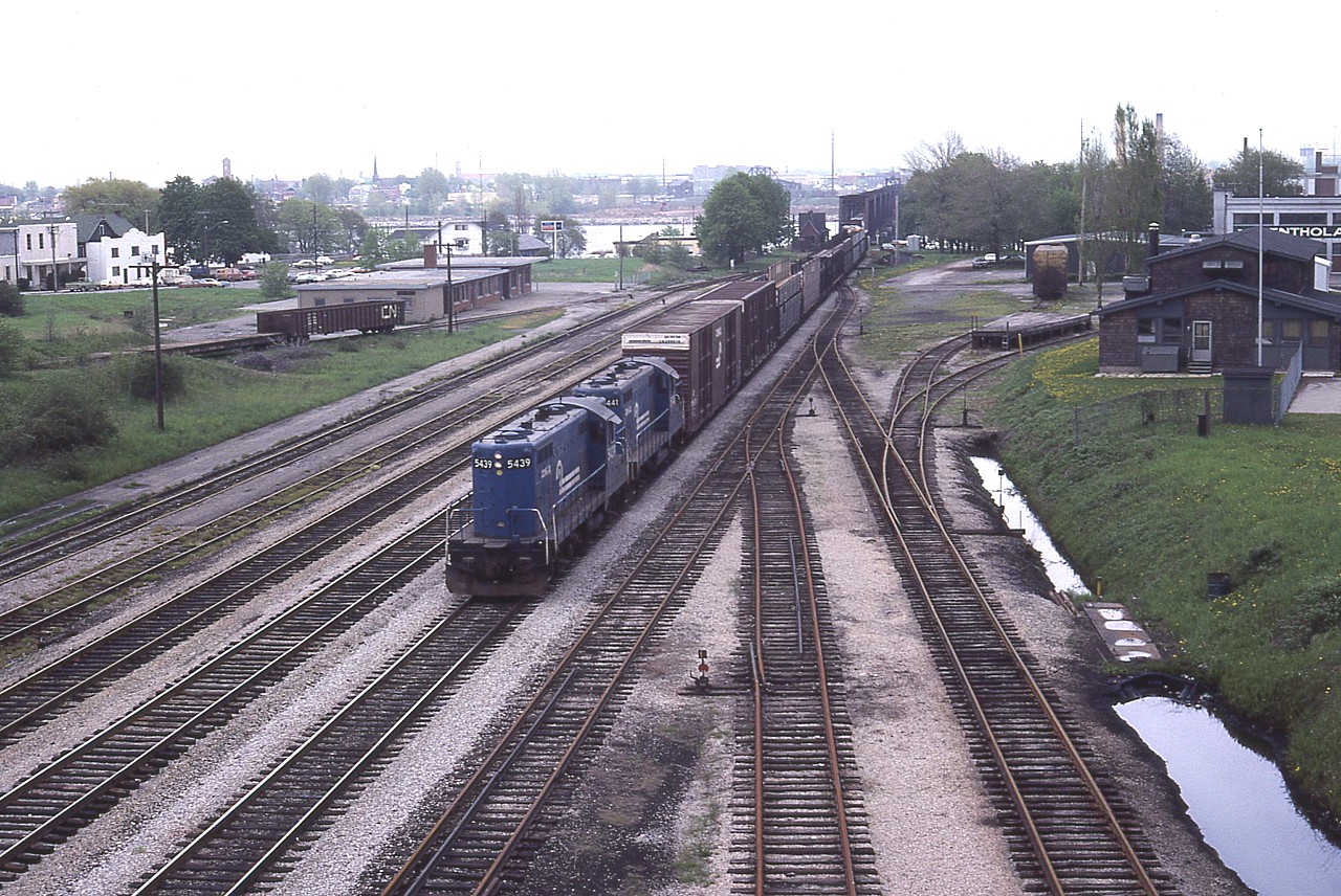 (Photo 2 of 2)  This is the Fort Erie complex area looking East from the Central Ave bridge. We see how much track there used to be here..........on the right was the lead to the old CN Dunnville Sub., also to the shop itself. On the left the MCRR/NYC track which led to Victoria Yd which was out of sight on the far right in the photo 1 of 2.  One gon on the track by the TH&B (MCRR) station, this building redundant after the last passenger (CP Budds) called here 04/1981 and was removed in the early 1990s. CR 5439 and 5441 are bringing in a transfer from the USA, they are on the CN yard lead. On the right, industrial stubs; there is a Boeing aircraft car back there, next to where the old GTR station used to be. By the bridge, Bridgeburg station is still there, known as B-1, built before Bridgeburg and Fort Erie (to the south) merged. B-1 moved to the Fort Erie Railroad Museum a mile or so away.  The crew hostel (aka: the Bunkhouse) for CN employees laying over was a popular place, nothing left there now but a cement pad........only about 4 tracks left here now and it is very quiet with only the odd trains, a few CP and the NS daily transfer using the line these days.