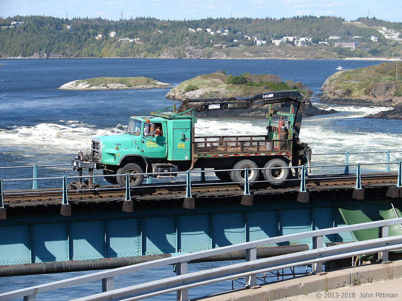 A New Brunswick Southern utility truck crosses the turbulent lower St John River on the ex-CP bridge. The reversing falls is just downstream (more like rapids when I was there, depends on the state of the tide). 
New Brunswick's Irving Corporation acquired the former CP (Canadian Atlantic Railway) network in New Brunswick, and operates it as the New Brunswick Southern Railway. They also have some lines over the border in Maine.