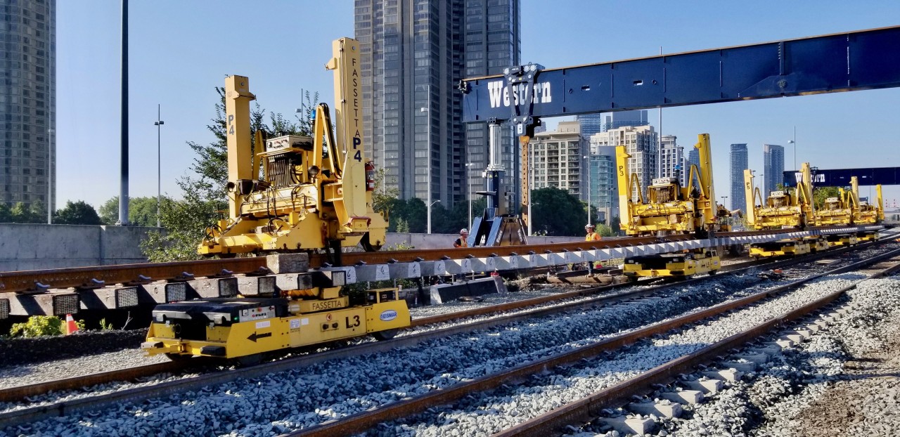 Absolutely amazing watching the process of rail replacement on the Oakville Sub at Humber.
The panel tracks for the approaches to the Humber are built off site, then loaded on these really cool remote controlled self propelled trolleys (8 in total). When the panel track is in position on the track next to the one being replaced, the robot gantries  that are sitting on top of the new rails put their arms down on to the ballast and lift the panel track up and off the dollies. Then the 8 trolleys are remotely removed from under the panel track. The gantries which can move vertically and horizontally now can move the panel track over towards the graded roadbed and set into place. Fascinating!!