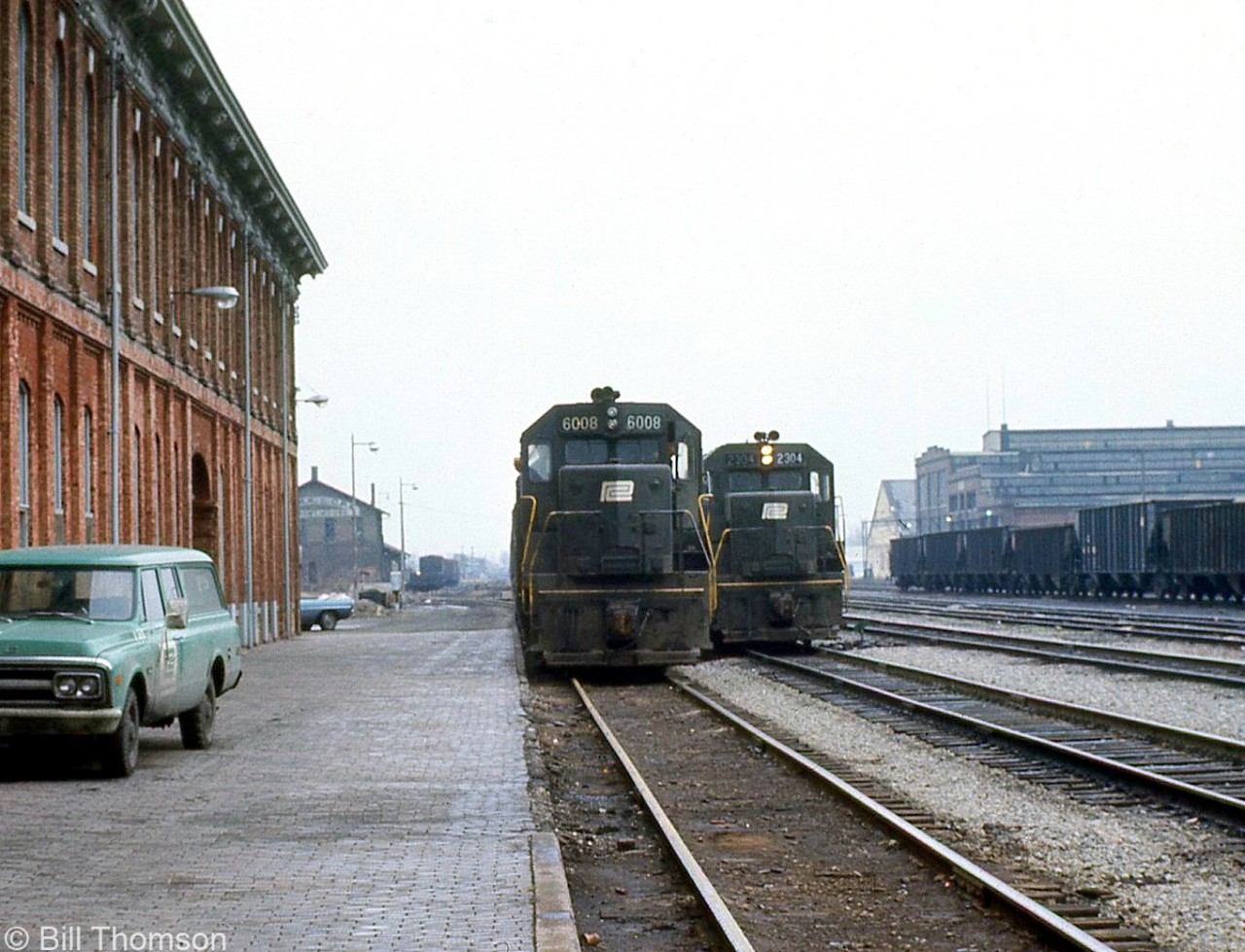 A view from the platforms of the old Canada Southern St. Thomas station one January day in 1973 shows westbound power posed by the station lead by Penn Central SD35 6008 and GP35 2304. A green PC vehicle is parked by the station, and behind in the distance is the old NYC-CPR freight house. Visible on the right beyond the cut of hoppers is PC's St. Thomas locomotive shops (originally built in 1913 by the Michigan Central RR). Today all the rails have been removed, but the station and shop building remain.