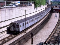 TTC H4 5594 (relatively new at the time, built by Hawker Siddeley Canada in 1974/75) leads a mixed train of H4's and four older H-series cars northbound out of Davisville Subway Station on the Yonge subway line, bound for Finch. An old Gloucester "G" train is sitting on platform 3, possibly waiting to enter service for PM rush hours, and a TTC bus (likely a GM fishbowl) is visible laying over in the bus bays of Davisville station. The lead car 5594 upon its retirement was converted into work car RT-64, and appears to still be on the roster. <br><br> Another interesting thing is the "Identra Coil" placed on the top corner of the lead car (sort of like an extra flag would be on a locomotive). Those were used to activate the Next Train sign boxes mounted on the ceiling at station platforms that would display the correct end destination or routing of an arriving train for passengers on the platform (if the train would be short turning, it would show the last station stop for example). One may still be able to find a few of those old sign boxes in place around the system, although by now long out of use. <br><br> <i> J. Bryce Lee photo, Dan Dell'Unto collection slide.</i>