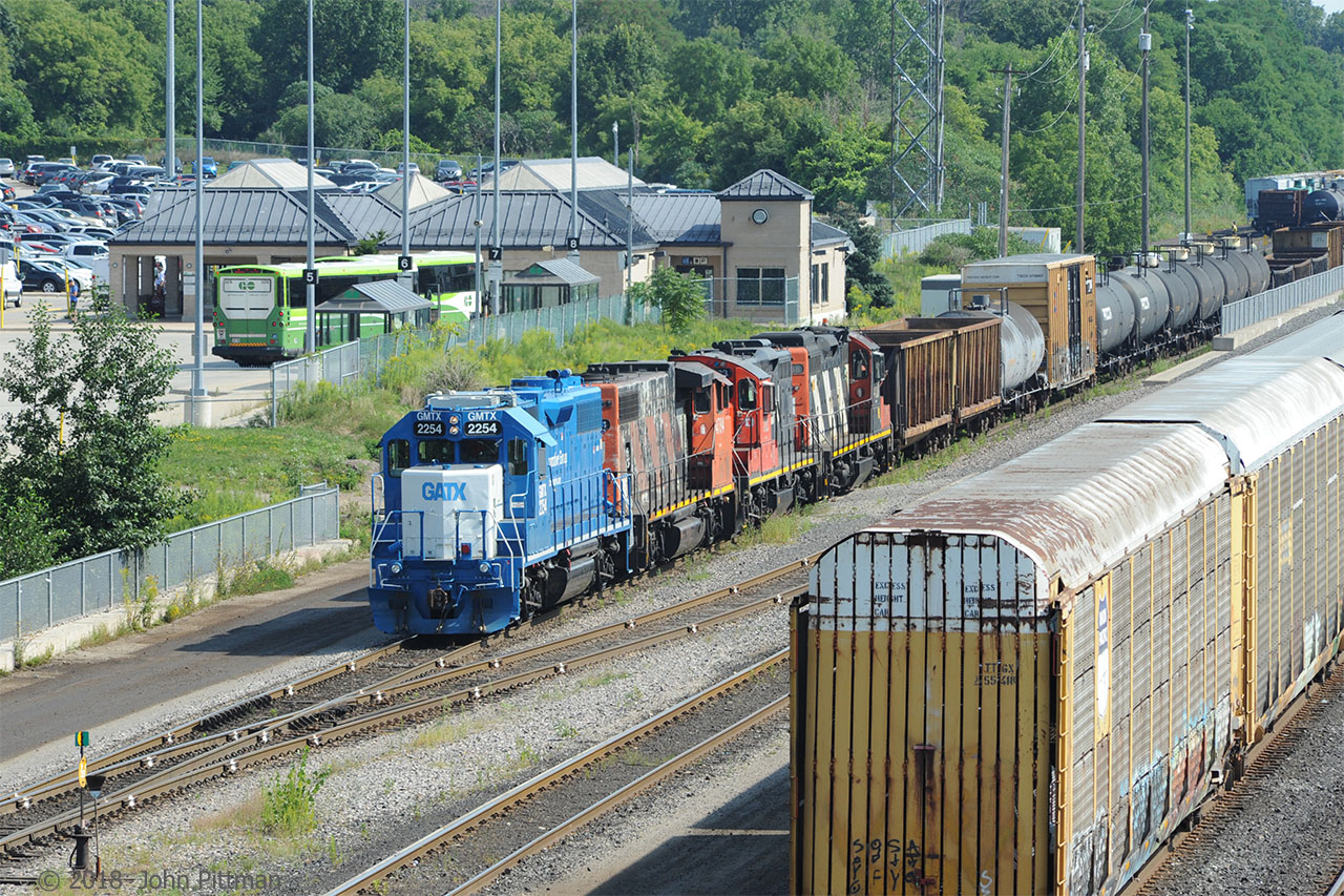 GMTX 2254 (GP38-2) works Aldershot Yard with the help of CN4784 (GP38-2W) and CN7083, CN4138 (GP9rm). It's the preferred cab on a hot summer day because it has air conditioning. The yard office can be seen partly hidden by the boxcar. Rail joiners have been highlighted with white paint. 
The engines are paused close to Aldershot GO/VIA station - platform access is through a tunnel under the yard (the south parking lot is closer). After Aldershot station was completed, VIA ended service to CN's Burlington, Dundas, and Hamilton stations.