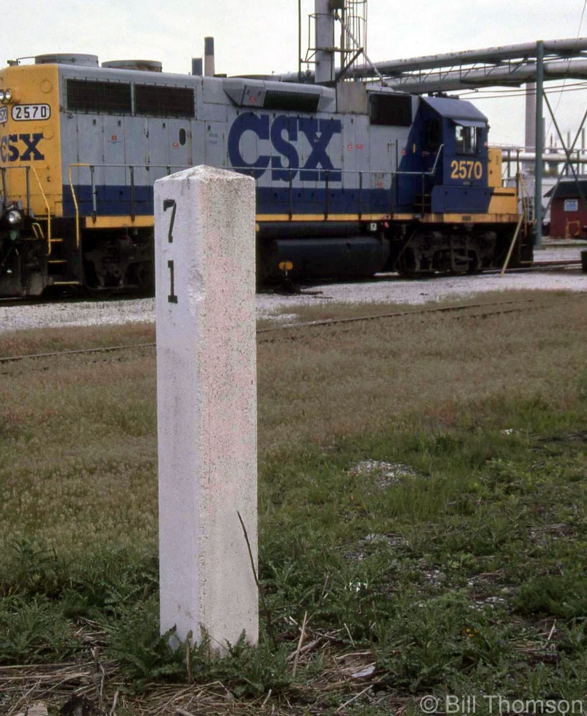 A white mile post marker marks Mile 71 of CSX's Sarnia Sub, adjacent to power parked at their engine shop facilities. The end of the Subdivision is half a mile north near where the line connects with CN.