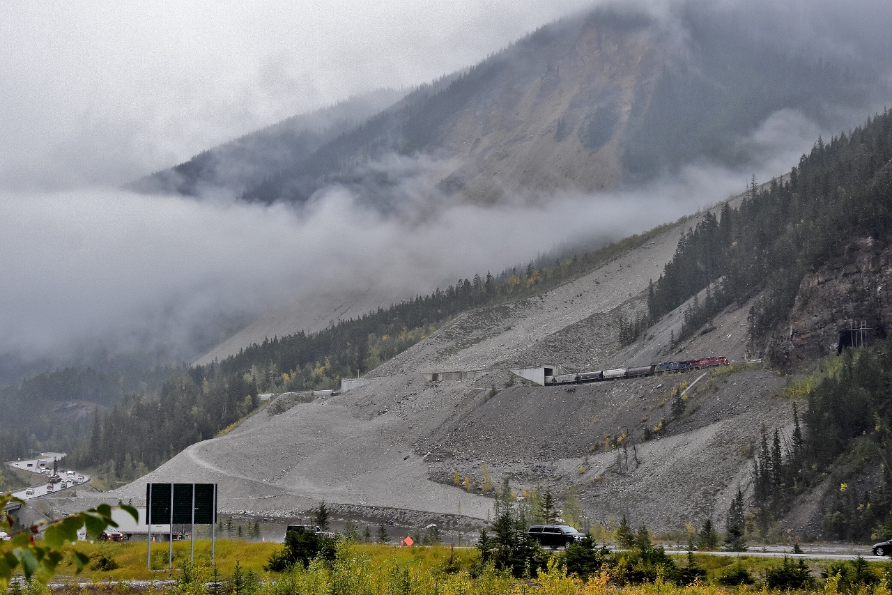 ...looking east up the Kicking Horse Canyon towards the Cathedral Craigs that is lost somewhere in the cloud and rain and snow....

 
...CP8960 (and CEFX1036) westbound on the downgrade approach to Field, B.C., with a loaded grain train at 20 mph....the tail end has likely just cleared the lower Spiral Tunnel....

 
September 14, 2018 digital in the B.C. Rain, at the Kicking Horse Canyon Flats,  by S. Danko.

 
What's interesting


….weather was miserable but notable on the B.C.  side of the Continental Divide plus 6c and rain, go east up the hill and over the pass and into Alberta the temperature was +1c and snowing.....

 
…the image's dominant feature is the Mount Stephen Glacier slide path, the site of many CPR incidents including wrecks due to material sliding onto the right of way....the lower portion of the Slide Path has been graded by the Trans Canada Highway maintenance crews to direct sliding material away from the River and the TCH...in fact it was the National Parks that asked CP to build the concrete snow sheds after the 1986 incident when 17 sulphur cars landed in the Kicking Horse River …. ( the River is between the CPR and TCH at the site of the slide path,  the TCH bridge over the River is visible extreme lower left corner).


On the TCH: up the hill, out of sight round the curve and in the cloud (fog) is the Spiral Tunnel Lookout – the view from such is 95% treed out, probably does not matter as the road widening will likely wipe out that lookout...

 
….plenty of 2018 – 2019 construction on the TCH east up to the Continental Divide to widen the road to four lanes, crews are literally blasting away half a mountain (on the north side) and at that point the CP is on the south side of the TCH...

 
...driving east up the TCH to the Kicking Horse Pass ( not visible in this image, elevation: 5,339 feet at Stephen, B.C. ) note that a portion of the TCH (above the Spiral Tunnel Lookout) is built upon the original CPR right of way – that grade would be just plain scary to put any train on......in any era..


..elevation between the Upper and Lower Spiral Tunnels near Yoho is 4,675 feet....and Field, B.C. Elevation is 4,121 feet

 
 ..that CEFX1036 unit been on CP over 15 years, got a shot of 1036 at Lovekin !  

 
Information credit: the book Nicholas Morant's Canadian Pacific: by J.F.Garden

 
note: Image captured from a public roadway

 
sdfourty