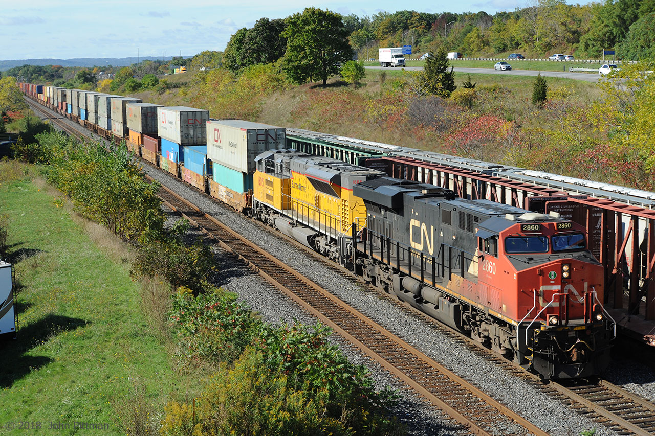 CN container train 148 has ES44ac CN 2860 in the lead. It's the second unit that is interesting - EMDX 1605, painted in Union Pacific colours, is one of EMD's Tier 4 demonstrator units. Hood-side lettering beneath ELECTRO-MOTIVE reads  THE NEXT GENERATION OF PROGRESS ## SD70ACe-T4 
While EMD has labelled the locomotive as a member of the SD70 family, the prime mover is very different. Apparently the 2-stroke EMD 16-710 diesel engine, as used in other SD70's, could not be adapted into a practical Tier 4 compliant engine.
Instead the locomotive is powered by a 12-1010J 4-stroke diesel engine rated at 4600 HP, developed from the 16 cylinder 265H 4-stroke diesel that was the intended power for EMD's SD90MAC-H. 
Web sources indicate that UP ordered 88 SD70ACe-T4 and has a number of them in service, while Norfolk Southern had 10 on order as of August 2018. 
There are 3 trains on the 4 tracks in this picture: Track 3 is unoccupied, CN 148 is on Track 2, CN 422 is on track 1, and CN 421 is on the Aldershot Yard west end lead.