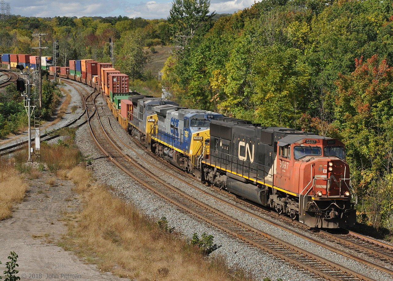 Eastbound CN doublestack container train 148 is a colourful sight as it sweeps around the S-curve at the west end of the Bayview Junction wye, approaching the Oakville Sub. Autumn colours are just starting to appear.
In the lead is GMDD SD75i CN 5697, with ex-CSX GE Dash 8-40CW lease units GECX 7353 and GECX 9142 following.
GECX 7353 has minimal patching; original CSX unit number with GECX stenciled below and a black line through CSX.
 GECX 9142 is more heavily redacted; different unit number and number boards, CSX totally blacked out.
Looks like the black paint over CSX and the cabside number was applied with a paint roller.
