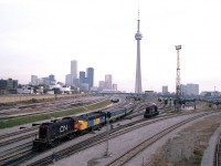  A panoramic view of the old Toronto core trackage and the VIA maintenance centre as it once was. Amazing numbers of rolling stock, amazing amount of track. Changes far to numerous to mention; lets just say we know where the financial district and the CN Tower are, and go from there. 
CN 8519, an employee of the VIA centre, is seen moving around VIA 6761 and its train. Other unit is unidentified. Not often did I use a 28MM wide angle lens with the old Pentax K-1000, as I did here.