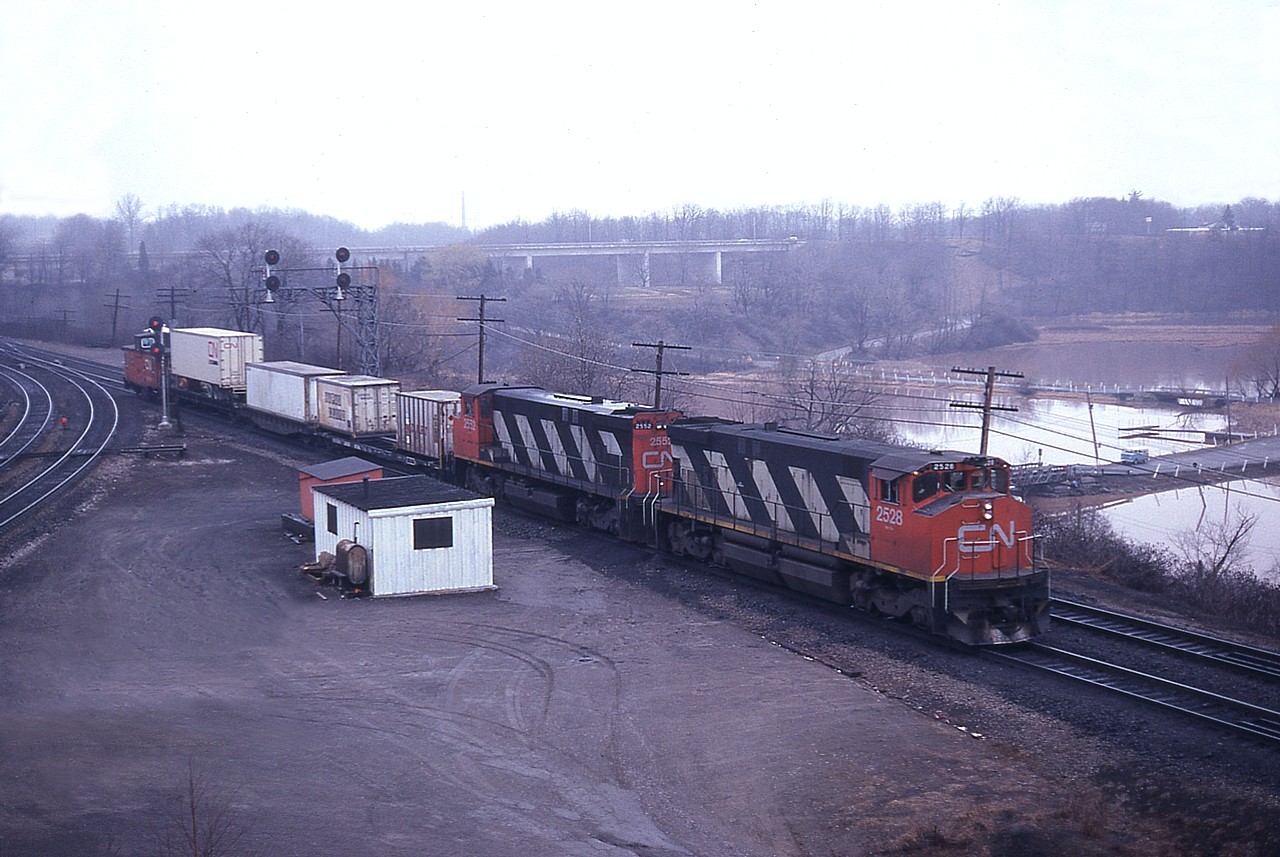 Perhaps someone can enlighten me as to when this particular container train ran. I believe it was a #154 that went Stateside from Mac, as shown here in its very early days. Obviously not long after start up; I doubt it ever ran much shorter than this.  CN 2528 and 2552 are power this day on their way to the USA via the Grimsby Sub. These  MLWs of the 2500 series were renumbered into 3500s by 1987, except a handful that were retired beforehand. The 2552 was retired in 1984, The other, as 3528, went to National Railway Equipment by 1998.