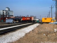 "Diamonds Aren't Forever": a sunny afternoon finds CP S2 7063 clattering across the West Toronto diamond with its train in tow, heading eastbound on the North Toronto Sub passing crews working at the interlocking plant (note all the green and red flats erected trackside). We're looking northwest along CN's Weston Sub to the diamond where it crosses the CP's North Toronto Sub at "the Junction", with the CP's Galt Sub-MacTier Sub connecting track that intersected both lines visible on the left.<br><br>Further in the distance behind 7063's train, one can see the (Old) Weston Road bridge that once carried automobile traffic over CP's lines (condemned to traffic and closed by this time, and removed later in the 80's). The old Maple Leaf Milling elevators and silos are also visible, once served by a lead that curved off CP and ran north to the elevators, where continued north along Cawthra Ave. and turned into a CN lead. In the background between the little S2 and the yellow CP Rail Ford "Louisville" work truck, one can see the red cab of a CN switcher parked at their own West Toronto freight yards that were once located near St. Clair Avenue and the nearby stockyard area.<br><br>Today, much in this scene is either gone or changed: the little Alco/MLW switchers have long been retired, the bridge and silos have been demolished, CN's yard is gone (CP's remains to the west), and the diamonds have been removed in favour of a grade separation for Metrolinx/GO Transit's commuter and UPX trains.<br><br><i>Charles Begg photo, Dan Dell'Unto collection slide.</i>