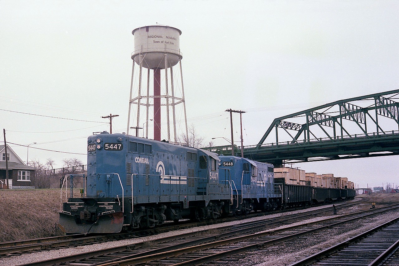 A few years ago I posted a shot of this train. This image, taken from the opposite side of the track,  I feel is a much better one. This is CR 5447 and 5448, fresh rebuilds, running on the former CN Dunnville line which enabled the power to wye the CN complex at Fort Erie after bringing over traffic to Canada. Shown here heading stateside by the Central Ave bridge, these locomotives after rebuild are designated GP8s rather than the GP7s they were originally built as. Whats in the gons? Someone had suggested they were crates of automobile parts from Tillsonburg area. Certainly a 'primitive' way of shipping compared with todays' standards.  
The track this train is running on as well as the adjacent was removed many years ago. The bridge was replaced recently. The water tower is long gone. No idea about the locomotives.