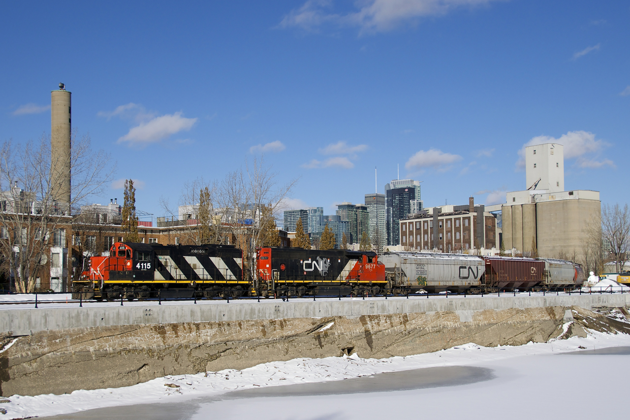 CN 4115 & CN 9677 shove 8 grain cars to Ardent Mill, visible at right. In the distance is the skyline of downtown Montreal.