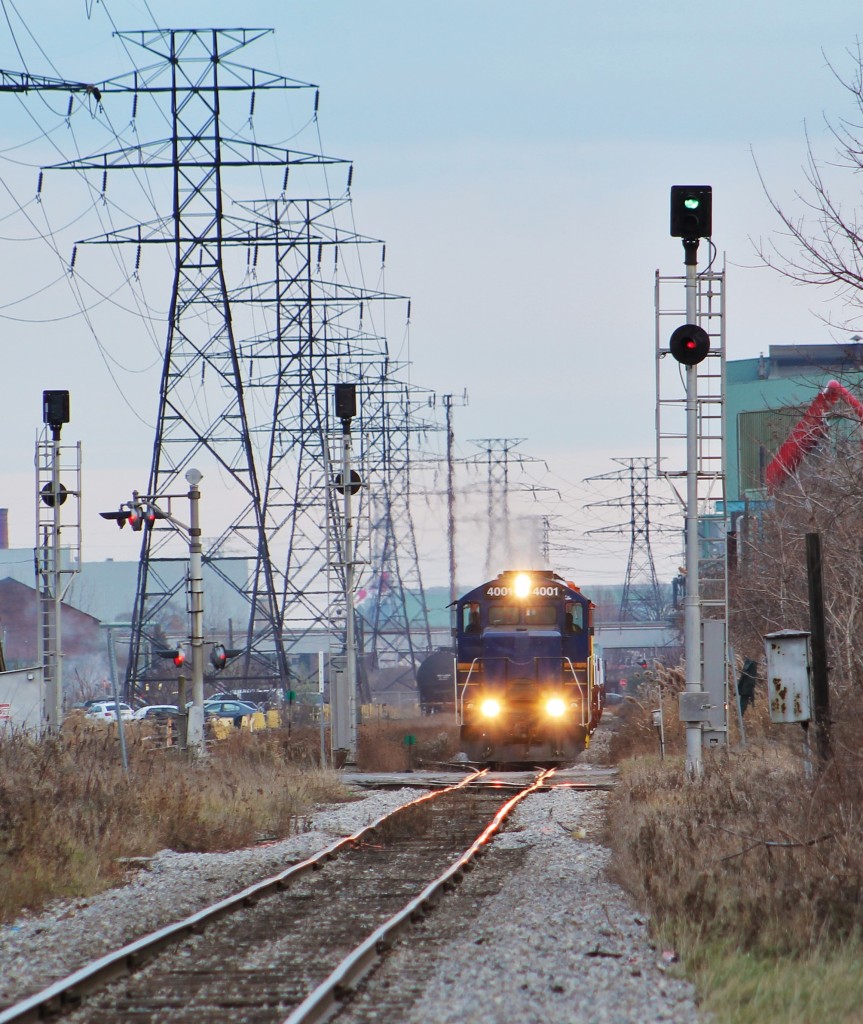 An SOR local heads back to Hamilton Yard after working various industries around the industrial area of Hamilton. The signals in the shot are for the diamond between CP and SOR at Gage Ave. They operate on a first come first serve basis. Basically, the signals are always green for all directions. When an approaching train reaches a certain point before another does, it will have the right of way through the diamond and all other signals will drop to red. Other trains have time to react to this because they're going at a speed which allows them to stop within half the distance that they can see. This is why the signal facing the camera is still green even though there is an obvious obstruction on the track ahead. I believe these signals are called ABS signals but feel free to correct me if I'm wrong. Pretty soon though shots of SOR here won't be possible with CN taking over operations in this area on December 18th.