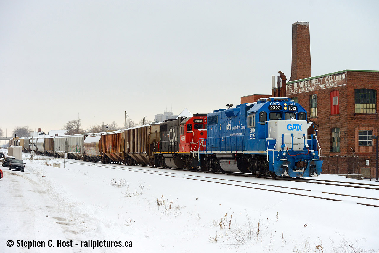 Here's the only train to be found with CN paint on the first day of CN's operations on the Guelph sub in 20 years, seen passing the Rumpel Felt Company building just west of the Kitchener station.

The way I see it, last trains and first trains run whenever they do, despite the weather. And I heard there was a flurry of activity at Kitchener just before Lunch so off to Kitchener I went to capture some shots (anything!) of the first day of CN's return to the area. Ultimately, today was a day of learning for everyone, new rules, timetables, signal testing between MX and CN at Sturm (new control point mile 65.1) and all kinds of delays. I'll try to tell some of the stories as I heard over radio and saw with my own eyes.
L540 was sent down the Huron Park Spur to work the Interchange and was set to meet L568 in the yard at Kitchener so some of these cars can be taken to Stratford. Metrolinx sent their Geometry truck down the line and took the Kitchener siding out of service completely, and at the time of this photo the Truck (As a foreman) was in Guelph heading east. Due to the way MX CTC or the TOP was set up 540 could not get any light until the truck was clear Hanlon, delaying 540 so I was able to make it here for a shot. L568 was patiently waiting in the yard, and at the same time A432 was on duty at the east end of Kitchener yard with QGRY 2008 and SLR 3806 looking to depart with about 60 cars. 568 wanted to go first but the Trainmaster wanted nothing to do with that. With 540 having the main track (Kitchener to Hanlon, remember, MX CTC is primitive!) 432 was going nowhere until 540 cleared, 568 got a clearance and departed for Stratford, and by then I had already went back to Guelph with a couple shots of this train, the only train with CN painted power to be found in daylight. 432 would depart around 2:30 PM with only the GEXR assigned motive power! To top it off 85 was delayed about 45 minutes due to signal issues at STURM and even called the CN RTC to note errors in the timetable/DOB and confirm speed limits. It's certainly been an interesting week. Corrections welcome of course.