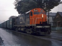 Street-running on a gloomy wet day, CN C424 3232 heads north up Ferguson Avenue on the Hagersville Sub in Hamilton, leading train #466 not far from arriving at Hamilton Yard. A nice selection of NYC jade green double door boxcars trails the power (perhaps one of the resident locals/experts knows what traffic they handled and from where). Judging by the "mountain" (Niagara Escarpment) in the background, the train has just come onto the street-running portion, not long after having descended the steep grade into the city. Pinpointing the exact spot today is difficult due to some of the housing along this stretch having been redeveloped, but I believe this is around Jackson Street or Main Street.
<br><br>
<i>Reg Button photo, Dan Dell'Unto collection.</i>