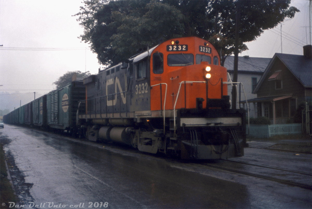 Street-running on a gloomy wet day, CN C424 3232 heads north up Ferguson Avenue on the Hagersville Sub in Hamilton, leading train #466 not far from arriving at Hamilton Yard. A nice selection of NYC jade green double door boxcars trails the power (perhaps one of the resident locals/experts knows what traffic they handled and from where). Judging by the "mountain" (Niagara Escarpment) in the background, the train has just come onto the street-running portion, not long after having descended the steep grade into the city. Pinpointing the exact spot today is difficult due to some of the housing along this stretch having been redeveloped, but I believe this is around Jackson Street or Main Street.

Reg Button photo, Dan Dell'Unto collection.