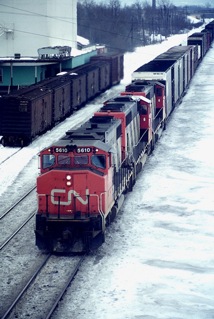 Rather than today's SD70I; CN 5610 back in 1976 represented the last in number sequence of the GP38-2 (W) series. Here is that GP with what appears to be two sisters running eastbound past the old Aldershot Cold Storage landmark. Not often did I see cars in the siding, but it appears in this image it 5 of the 6 are reefers from Northern Refrigerator Car Company.  The GP38-2(W) still toils on CN, but now as 4810 when the series was renumbered back in 1988. The cold storage building, constructed in the 1930s for use by farmers for storage and shipping, was knocked down about 10 years ago.
Photo taken from Waterdown Rd bridge, back when that road was relatively quiet.