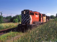 CP GP30 5001, running long-hood-forward, and van 434020 prowl weed-grown trackage with a single bulkhead flatcar in tow, passing through Belwood westbound on CP's Elora Sub. The Grand River is a stone's throw away and runs along this portion of the line (which crossed over it to the west at Shand Dam) but is obscured from view by the foliage. I initially thought the train was traversing the passing siding at Belwood, but according to track diagrams the closest weed-ridden track the train is on is apparently the mainline.<br><br>GP30 5001 (one of only two CP GP30's and the only ones built in Canada) had been recently retrofitted with a rear pilot, rear markers and rear numberboards as part of CP's DRF to DRS converion program for its GP30, GP35 and C424 fleet, in order to boost ranks of 4-axle roadswitchers in light of the bulk of their GP9's being rebuilt as yard units. The rear features were required for leading trains in branchline service on lines that might not have turning facilities but warranted only one unit. All three groups would become common branchline power on CP in the 80's and 90's, along with rebuilt RS18u and GP9u road switcher units. <br><br>One of the many "Bruce Branches" that once spanned the area, the 29-mile Elora Sub split off from CP's Orangeville (Owen Sound) Sub at Cataract, and ran 29 miles west via Erin, Hillsburg, Belwood, and Fergus to Elora. According to a CP timetable, in 1980 the Elora Sub was listed as 25mph maximum operating speed with some 20mph portions, but by the mid-late 80's the line had deteriorated to 15mph speed with 5-10mph speed restrictions along most of its light 72-100lb rail (not suitable for cars over 220k lbs according to special timetable instructions). Traffic along the line had also all but dried up in that time. As was the fate of many other unprofitable branchlines, CP applied to abandon the Elora Sub and received approval in December 1987, and that was that. One can still traverse its former right-of-way today as the Elora Cataract Trailway.<br><br><i>Keith Hansen photo, Dan Dell'Unto collection.</i>