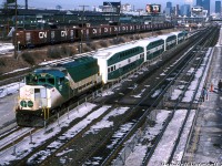 GO GP40-2W 707 with a short consist of four bilevels plus an APCU stops at Exhibition Station to pick up passengers on the westbound platform, as passengers wait across the tracks on the eastbound platform for their train heading downtown. This was shot from the pedestrian bridge that used to span the platforms, looking east to Bathurst Street and the downtown core visible in the distance. On the left is the Liberty Village part of Toronto, an industrial manufacturing sector of the city that, at the time of this photo, had seen better days and was in decline as manufacturing moved out of the downtown core. A string of classic CN 40' boxcars populate the storage tracks in front of one of Loblaw's former warehouses (off Colt Street).<br><br>In the background the old Inglis plant and its iconic billboard sign is visible at CN's Fort York interlocking by Cabin E (still there, hard to pick out), that once protected the CP's old TG&B "Wharf Lead" which came down from Parkdale Yard and crossed each of the CN mainlines with a diamond (replaced with crossovers the previous year). Large billboards promote the Blue Jays and Canon calculators to passersby on the elevated Gardiner Expressway (out of frame to the right). On the far right is one of the few old CNE storage tracks at the east end of the platforms, with others nearby on the other side of the fence. Needless to say, most of this is very different today!<br><br><i>Keith Hansen photo, Dan Dell'Unto collection slide.</i>