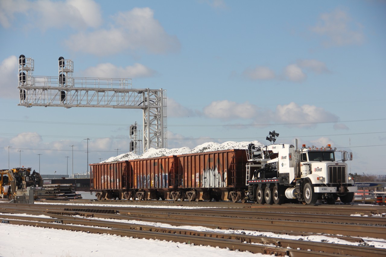 A CN/Brandt powered ballast train sits atop the bridge over Thickson road in Whitby. The work train will proceed just east of thickson road where an excavator will begin unloading the snow coloured ballast from the top of the cars. Work on the GO line here is part of the GO,s maintenance facility with new track and signals.
