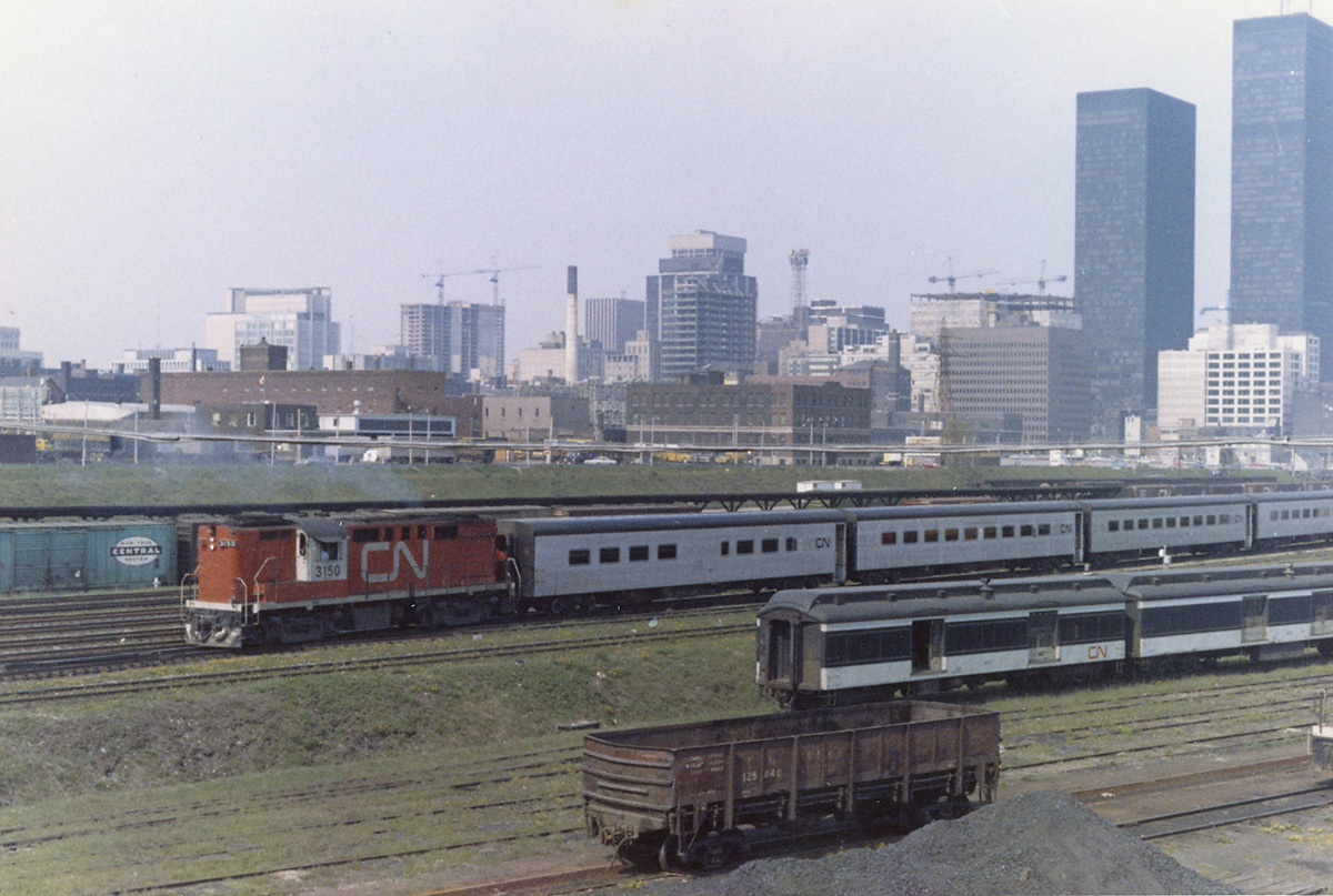 A Tempo consist backs towards Union station from Spadina.  I'm guessing it's backing up from the exhaust.  Lots of cranes at work on the Toronto skyline, and I love the old baggage cars!