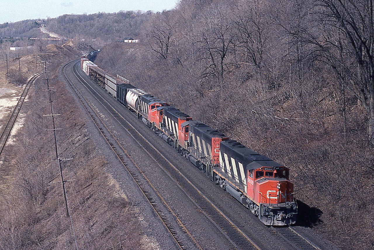 This is one healthy looking eastbound freight, as seen from up in the old Canada Crushed Stone Conveyor that used to stand over the CN main line at Mile 4.(This structure was dismantled in 1986) Four GP40-2(W) locos, the pride of the roster back then, CN 9609, 9584, 9548 and 9603 have a train that stretches past the old Dundas station and well up the line past the Mile 5 marker. My notes indicated a car count of 127. On the left can be seen the connection to the lower CCSL and Steetley dolomite property (removed in Oct '85) and on the right in the brush one can see where track went up to the CCSL loading area.