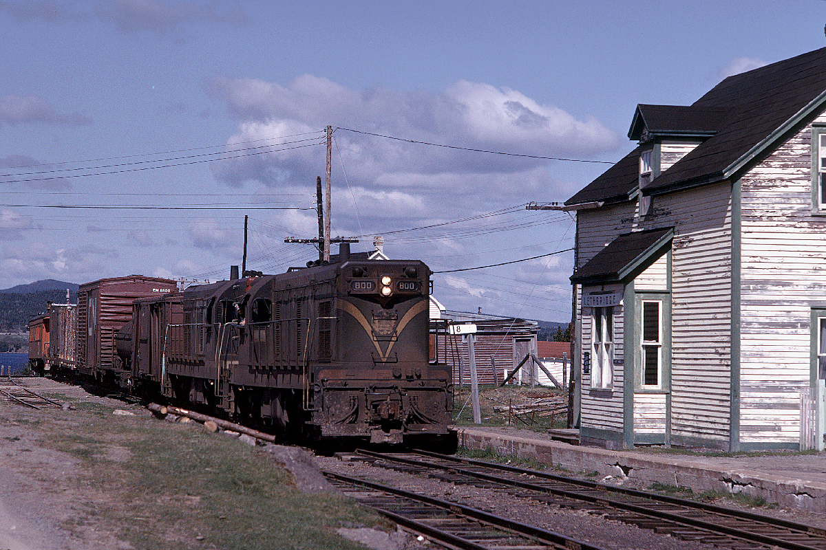 CN Mixed Train 205 pulls to a halt at Lethbridge, Mileage 18 of the Bonavista Branch in central Newfoundland.  At this time in June 1973 the train was scheduled to leave Clarenville at 8 a.m. on Monday, Wednesday and Friday for the four hour and twenty-minute, 80-mile run to Bonavista.   It was scheduled to return later the same day at Train 206.  My wife, Judy and I chased this train as part of our Honeymoon Trip to Newfoundland and Labrador.  Kindly engineer Bill Mornell told me how to access the Trinity Loop and paused while I clambered up and down the hillsides to get the best angles.  Later while we chatted in Bonavista, he learned that Judy had never been in an engine and so paused some miles south of town on the return trip.  He then made sure that she had a good long ride on the way back to Clarenville. G8a 800 had a long history on the former Newfoundland Railway.  It was built by GMDL in London in June 1956 and traveled by rail to Halifax where it sailed aboard the SS Random for Agentia.  It was placed in service by August.  The six G8s were double-headed with CNR steamers on the CARIBOU for a period prior to the arrival of the six steam generator units later that year. The G8s settled on the branchlines to Bonavista, Argentia and Carbonear where they ran in pairs and trios.  The 800 was retied in December 1986 and scrapped at Whitbourne in 1988. For more images from this and other chases on the Bonavista branch and throughout Newfoundland may I suggest that you contact me at bill.linley@gmail.com to obtain a copy of my upcoming book “Trackside Newfoundland.”