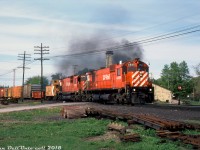 Big M's doing what they do best: smoke it up while hauling freight. CP M630 4569 leads C630M 4504, on what could be the London Pickup, possibly doing setoff work at Woodstock (the slide notes this as an eastbound train, but the power is facing westbound and coupled onto the caboose-end). This was taken from the now-removed Drew St. crossing, and the semaphore signals of Woodstock Station and adjacent lighting tower are visible in the background behind the train.<br><br>The bulk of CP's M630 fleet including 4569 were specially purchased for unit coal train service out west in 1969-70, partially due to CP's dissatisfaction with their GMD SD40 fleet at the time, and partially because of some of the features MLW offered including a better wheelslip system and more robust traction motors. The M's were separated into a few different number blocks depending on features (notably Locotrol Master, Locotrol Repeater, and pacesetter equipment. Some were also renumbered when features changed). However, their coal train reign only lasted a few years due to reliability isues arising and higher-than-anticipated maintenance costs. When GMD released their new and improved SD40-2 model, CP found it to their liking, and by the mid-70's the big M's were bumped out of coal service and sent east to be maintained out of St. Luc for general freight service, as evident in this photo. The earlier M's like C630M 4504 had also been assigned out west (while they weren't Locotrol equipped, they were often used as trailing or mid-train robot-controlled power on unit coal trains, as well as seeing normal freight use).<br><br>The end came in the early 90's when the last of CP's big 6-axle MLW's were retired. Some were unretired due to a power shortage in 1994, but re-retired a year later. The smaller 4-axle MLW's including the C424's and RS18u's lasted a few years longer until the remaining units were retired in 1998.<br><br><i>Gord Taylor photo, Dan Dell'Unto collection side.</i>