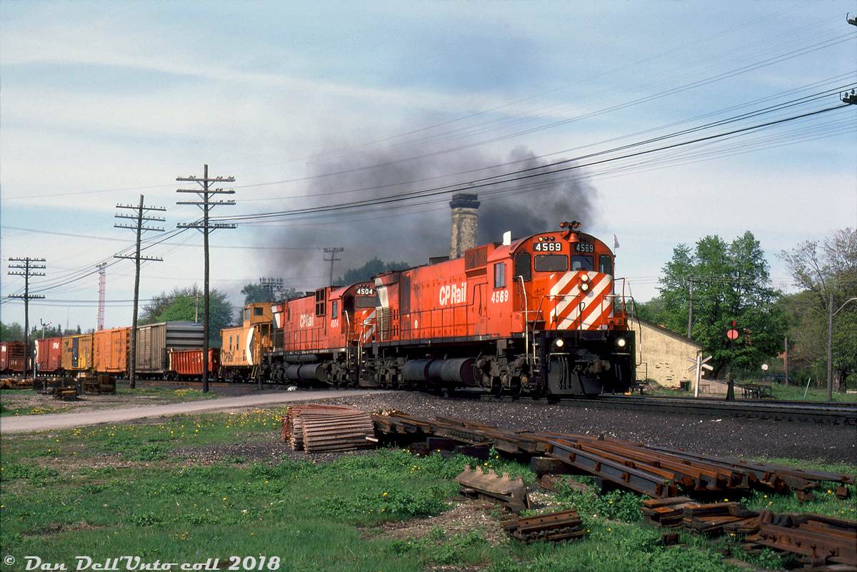 Big M's doing what they do best: smoke it up while hauling freight. CP M630 4569 leads C630M 4504, on what could be the London Pickup, possibly doing setoff work at Woodstock (the slide notes this as an eastbound train, but the power is facing westbound and coupled onto the caboose-end). This was taken from the now-removed Drew St. crossing, and the semaphore signals of Woodstock Station and adjacent lighting tower are visible in the background behind the train.

The bulk of CP's M630 fleet including 4569 were specially purchased for unit coal train service out west in 1969-70, partially due to CP's dissatisfaction with their GMD SD40 fleet at the time, and partially because of some of the features MLW offered including a better wheelslip system and more robust traction motors. The M's were separated into a few different number blocks depending on features (notably Locotrol Master, Locotrol Repeater, and pacesetter equipment. Some were also renumbered when features changed). However, their coal train reign only lasted a few years due to reliability isues arising and higher-than-anticipated maintenance costs. When GMD released their new and improved SD40-2 model, CP found it to their liking, and by the mid-70's the big M's were bumped out of coal service and sent east to be maintained out of St. Luc for general freight service, as evident in this photo. The earlier M's like C630M 4504 were also assigned out west during this time for general freight service (they weren't Locotrol equipped, so were often used as trailing or mid-train robot-controlled power on unit coal trains).

The end came in the early 90's when the last of CP's big 6-axle MLW's were retired. Some were unretired due to a power shortage in 1994, but re-retired a year later. The smaller 4-axle MLW's including the C424's and RS18u's lasted a few years longer until the remaining units were retired in 1998.

Gord Taylor photo, Dan Dell'Unto collection side.