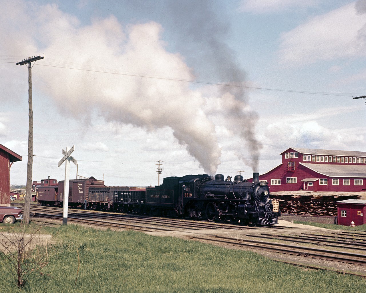 In the latter part of the 1950s, in the Upper Ottawa Valley community of Pembroke, Ontario, Stephan Delmonte (Del) Rosamond made a point of being trackside to photograph steam locomotive operations on Canadian Pacific Railway at a time when the Company was transitioning away from venerable steam power to modern diesel-electric locomotion.  The accompanying two photographs were archived during this time period.




On what appears to be a pleasant spring day, circa 1956-57, Del is on location near the downtown CPR station, as the Chalk River to Smiths Falls wayfreight makes a switch move in front of the Consolidated Paper and Lumber Company mill located on the south shore of the nearby Ottawa River.  Today's motive power is G1s class 4-6-2 Light Pacific No. 2219.  The engine, one of 39 coal fired G1's operated by the CPR, was out-shopped in February 1910 by Canadian Pacific's Angus Shops in Montreal, and has been modernized over the years.  According to the late Duncan H. du Fresne - who fired this class of locomotive - the engine received a new boiler and cylinders during a 1924 rebuild, and has been fitted-out with a modern cross compound air compressor.  In 1950 it became one of three G1 class 2200s to receive a Standard HT-1 Stoker, with the other 36 remaining hand-fired coal burners.  At the time of the stoker installation the engine was paired with a 14 ton/8000 Imperial gallon capacity tender.  Duncan would later write in his book titled 'When Steam and Steel get in your Blood' that “the upgrade made them into super G1's... much like the modern G5's".




Engine No. 2219 saw service in Eastern Ontario well into 1960, and was disposed of by Canadian Pacific in July 1961.  The locomotive was likely scrapped shortly thereafter.


Original digital scanning provided by DigMyPics in Arizona.


Additional Photoshop restoration by Raymond Farand.


Research and narrative courtesy of Raymond Farand.