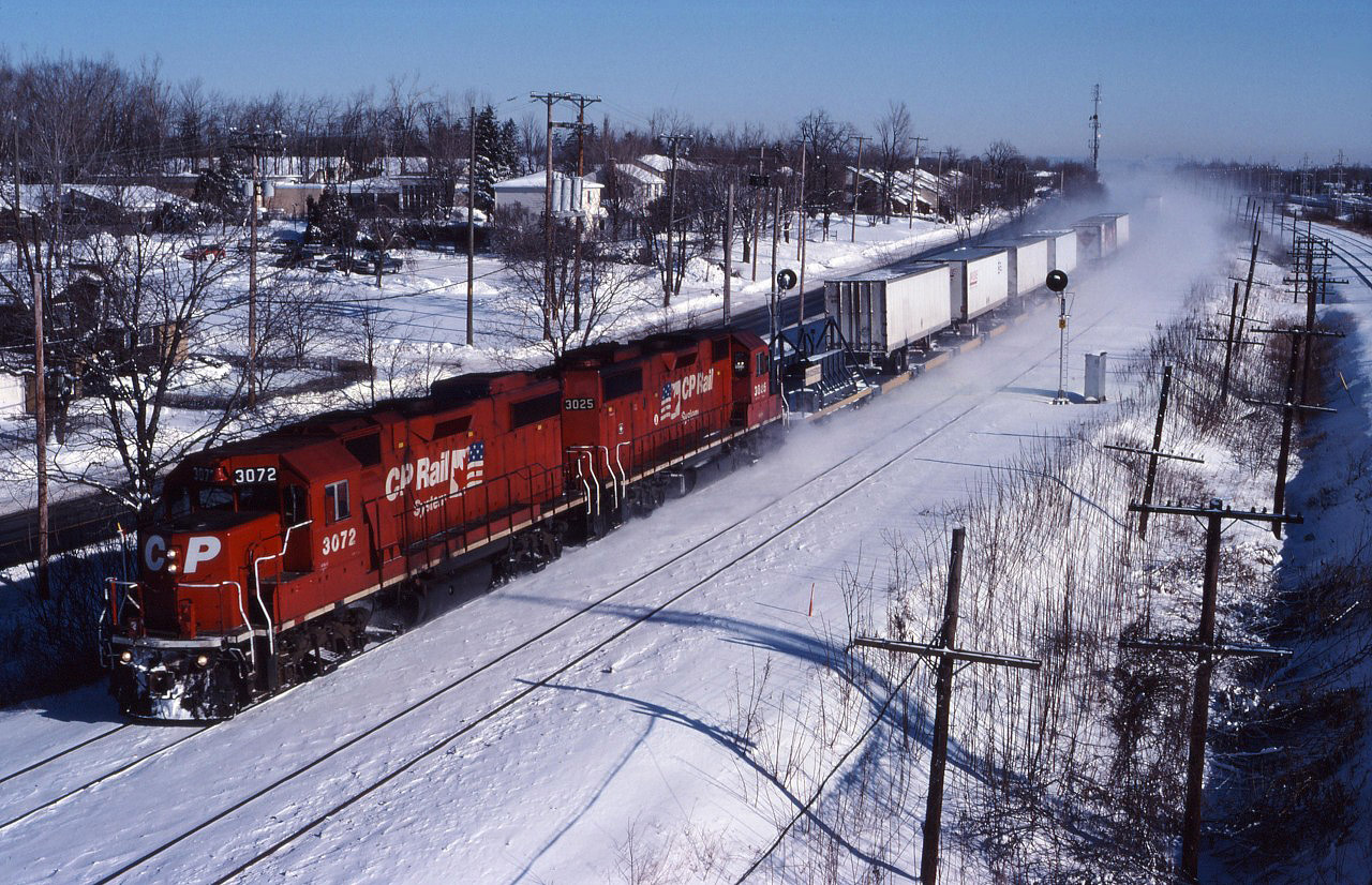 In the early days, CP's "Expressway" service ran behind GP38-2 units with "Iron Highway" technology. Snow kicked up by the westbound train hides the Beaconsfield commuter station as the train passes under the bridge near Beaconsfield High School on a cold January day.