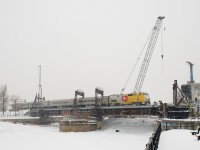VIA 34 with VIA 920 and four HEP cars crosses the Lachine Canal on a snowy afternoon in Montreal. In the background, preparatory work for the REM (Réseau express métropolitain) light rail project has begun.