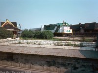 GO Transit GP40TC 9806, freshly rebuilt by CN at Pointe St. Charles shop in late 1974 and repainted in the new green and white livery, is seen pulling a train of GO single-level Hawker Siddeley cars westbound on the Weston Sub past both CN's Parkdale Station and CP's Parkdale Station. The busy Queen Street underpass (subway) is visible in the foreground - note the cutout in the stone retaining wall that lead to a stairway up from sidewalk to platform level. Freight yards belonging to both railways were also located here at the time, along with numerous industries and sidings that still received rail service.<br><br>According to another slide I have, this was shot right after a short CN passenger train (likely #161, CN still ran some passenger services up the Weston & Newmarket Subs but the only ones scheduled to stop at Parkdale were 160 & 161) had made its station stop at Parkdale, so going by timetables this is likely evening GO train #997 seen at around 5:43pm. GO's Georgetown line began service the previous year but Parkdale Station was never a stop for any GO trains (GO built their own station to the north at Bloor Street), so this GO could be either passing by or held up waiting for a light (perhaps the CN train was held up ahead at the diamond for a CP freight, or it was stopped at CN's West Toronto station). Despite this, Parkdale was a junction point between the Weston & Newmarket Subs so scheduled GO train times by the station were still listed in CN's employee timetables.<br><br>Both Parkdale stations had seen better times at this point, and were in their final years of existence: <br><br>CNR's Parkdale station (once known as "North Parkdale") was built in 1878 by the Northern Railway and expanded over the years. When closed the next year in 1976, CN wanted to demolish it (of course) but through fundraising by the Parkdale Save Our Station Committee the station was moved to Sunnyside in early 1977. Unfortunately a fire was started inside by vagabonds, and what was left was demolished that October.<br><br>CPR's Parkdale station (located directly across from CN's on the Galt Sub) was originally built in 1910, closed in 1968, and is seen here boarded up and out of use. It was finally demolished sometime in the late 1970's. It also had a stairway leading up to it, via an arch cut into the retaining wall <a href=http://www.railpictures.ca/?attachment_id=31661><b>off Dufferin Street</b></a> leading up to platform level.<br><br><i>Photographer unknown (possibly a Charles Begg slide), Dan Dell'Unto collection.</i>