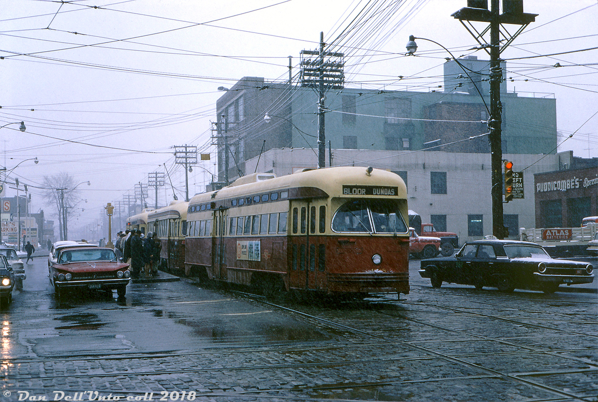 A snow/sleet mix appears to be falling on this mid-April (!) Saturday, as passengers crowd the streetcar platforms at the corner of Dundas Street West and Bloor Street West waiting to board a streetcar and get out of the weather. TTC A-13 class PCC 4738 (a former Birmingham car purchased secondhand) leads the pack signed up for the Dundas route, turning from northbound Dundas to westbound Bloor on a diversion west to Park Loop (once located at the north end of High Park off Bloor) during construction of the nearby Dundas West subway station on the yet-to-be-opened Bloor Danforth line. Other photos taken by Mr. Bromley that day show some Dundas streetcars were still looping at nearby Vincent Loop, so this may have been a Runnymede branch car only going as far as Bloor and diverting. Puddicombe Motors is pictured on the right at the southwest corner of the intersection (a large local Ford/Mercury dealer in the area). And, note that stylish 1960's Buick on the left!

John F. Bromley photo, Dan Dell'Unto collection slide.