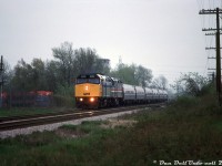 A gloomy Saturday evening finds VIA train #99, the US-Canada "Maple Leaf", heading westbound through Stoney Creek bound for Hamilton and Toronto. VIA F40PH-2D 6423 leads an Amtrak F40 (likely 296) and six Amfleet cars, passing by the old Waxman's scrap yard tower just west of SNS Stoney Creek where the Beach Sub once came off the Grimsby Sub near the hydro corridor. This was most likely taken from behind one of the lots off Cascade Street along the tracks, and if running on time would have been around 7:22pm going by the timetable. It's important to note that due to directional running at the time, this train was known as westbound #99 on the Grimsby Sub, and became #98 at Hamilton for running east to Toronto on the Oakville Sub (similarly, #97 from Toronto became #96 for Niagara Falls at Hamilton).<br><br>Much thanks to Mr. Mooney for helping pinpoint where this was shot from, and helping sort out the power (Bill had this one mislabeled as the earlier eastbound #97, which had run with VIA 6423 and Amtrak 348. A VIA unit was apparently used to assist a few trains around that time, and would often be turned in the 'falls).<br><br><i>Bill McArthur photo, Dan Dell'Unto collection.</i>