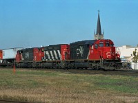 A CN eastbound with piggyback highway trailers (TOFC) on the front end is approaching Rectory Street grade crossing in London. The spire of St. Mary's Parish RC church crowns the first of three SD40-2 variants. CN 6018 is an SD40-2Q remanufactured from CN 5166, in its original CN North America paint scheme, while the others two are SD40-2w. <br>First trailer says "CN Piggyback" - don't know what percent of the train was piggybacks. <br> With some detective work I figured out the location and church. The date is more elusive. References indicated CN 6000-6028 remanufacture program was in 1993, while CN North America began mid-1992.  If anyone knows when CN 5345 got its CNNA repaint, when CN stopped Piggyback services through London, or the train number, please let us know in a comment.