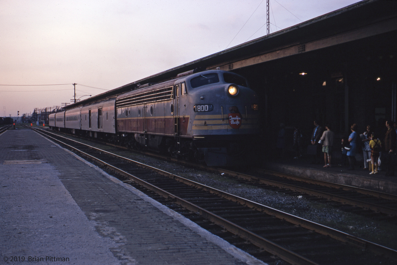 Classic EMD E8A CP 1800 leads a Quebec City to Montreal (westbound) passenger train into Trois-Rivieres station in the twilight of a summer evening circa 1970.  I was a passenger on this train, returning to T-R after a family day trip (by car) to Quebec City.  I can thank my father for the train ticket and photo. Trois-Rivieres is approximately the mid-point of this former St. Lawrence north shore train service. Dwarf and mast signals can be seen behind the train. The between-tracks platform was no longer in service, its canopy removed.
During 1970 and into 1971, either CP 1800 or 1802 frequently powered Passenger services on this line, otherwise a single FP7A or FP9a. I used to wonder about CP 1801, but it had been in a crash at the end of 1968. A dual-diesel E8A powering up and departing sounds great, standing alongside under the platform canopy. One of CP's earliest mainline diesels, the EMD builder plate showed 2250 HP, 1949 built. Some Alco yard switchers seen in T-R were even older.
Some time in 1971 the passenger trains on this line got converted to sets of RDC "Dayliners".