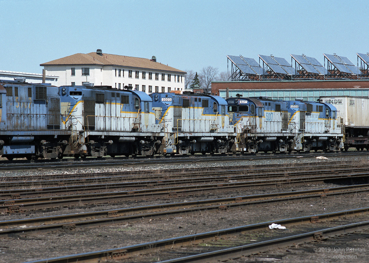 Five retired D&H locomotives follow behind the active units on a westbound CP train, lead by SOO 763 (SD40-2) and HATX 517 (GP40-2). Photographed toward the west end of CP's Quebec Street Yard, near the landmark military heritage T-Block building.
D&H 5000-5011 are RS-11, while D&H 5012-5023 are RS-36. Other than high/low short hoods not much visible difference, all have Alco 251 V12 prime movers of 1800 HP. Blue DH5002, then DH50??, DH5023, DH5017, DH5009 with a piggyback trailer on flatcar (TOFC) beginning the train.
CP acquired the D&H in 1992; online sources indicate that these engines were sold to NRE in 1993, with most of them scrapped. Looks to me like they are en route west to NRE in Silvis IL.
DH 5017 was saved, it is running in fresh D&H colours on the Delaware & Ulster tourist railway of Arkville NY (as of 2018).