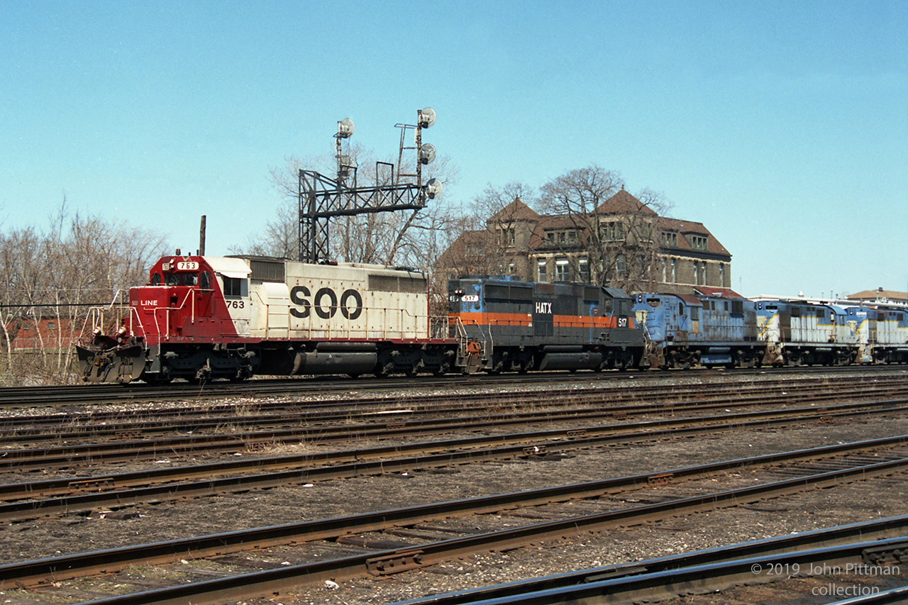 A westbound CP train, lead by SOO 763 (SD40-2) and HATX 517 (GP40-2 in Guilford grey over B&M blue), was seen toward the west end of CP's Quebec Street Yard, beside the landmark military heritage T-Block building built 1888 as the London Infantry School. 
What interests me about this train are 5 derelict D&H Alco RS-11 and RS-36 locomotives that follow. CP acquired the D&H in 1992; online sources indicate that these engines were sold to NRE in 1993, most of them getting scrapped. Looks to me like they are en route west to NRE in Silvis IL.