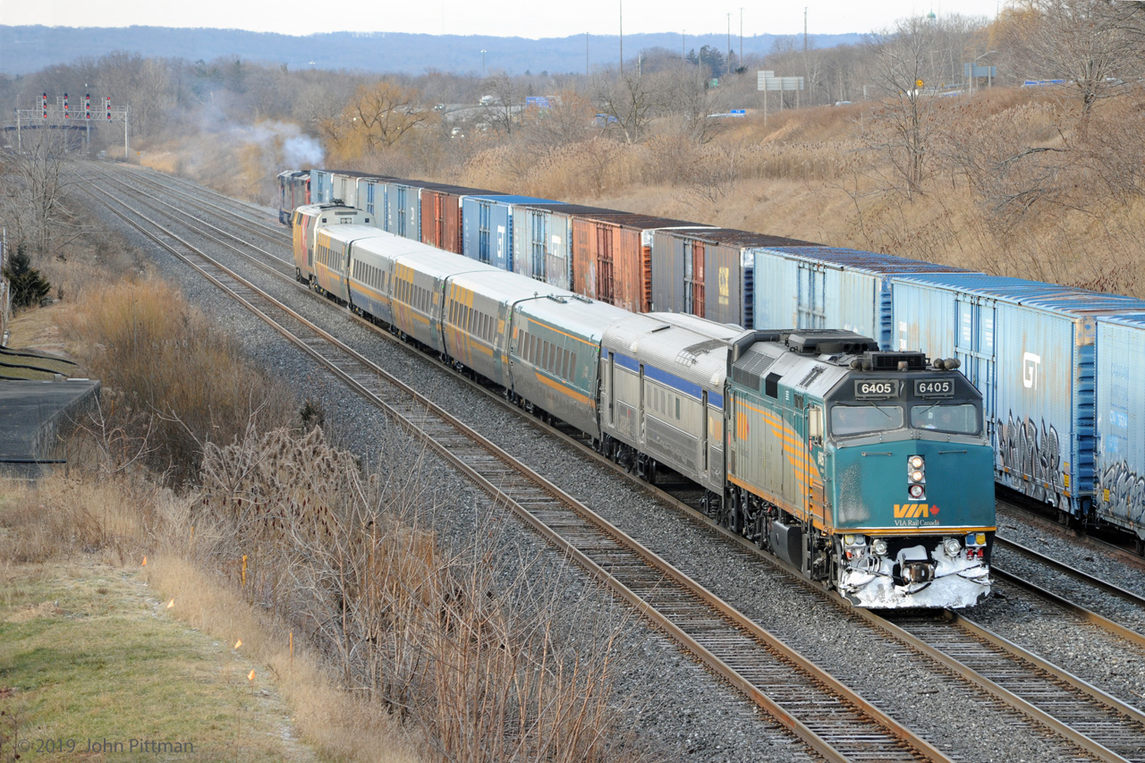 VIA train 70 (Windsor to Toronto), in a mix of colour schemes, is approaching Aldershot station on a cold winter morning. GMD F40PH-3 VIA 6405 leads a stainless steel baggage coach, 5 LRC coaches, and GE P42dc VIA 916 pushing.  Meanwhile CN train 421 (Macmillan Yard to Port Robinson) is on its way out of Aldershot Yard, easing down toward CN Snake to await its signal. CN 421 is powered by back-to-back GE Dash 8-40CM Draper taper cowls CN 2424 and CN 2436.